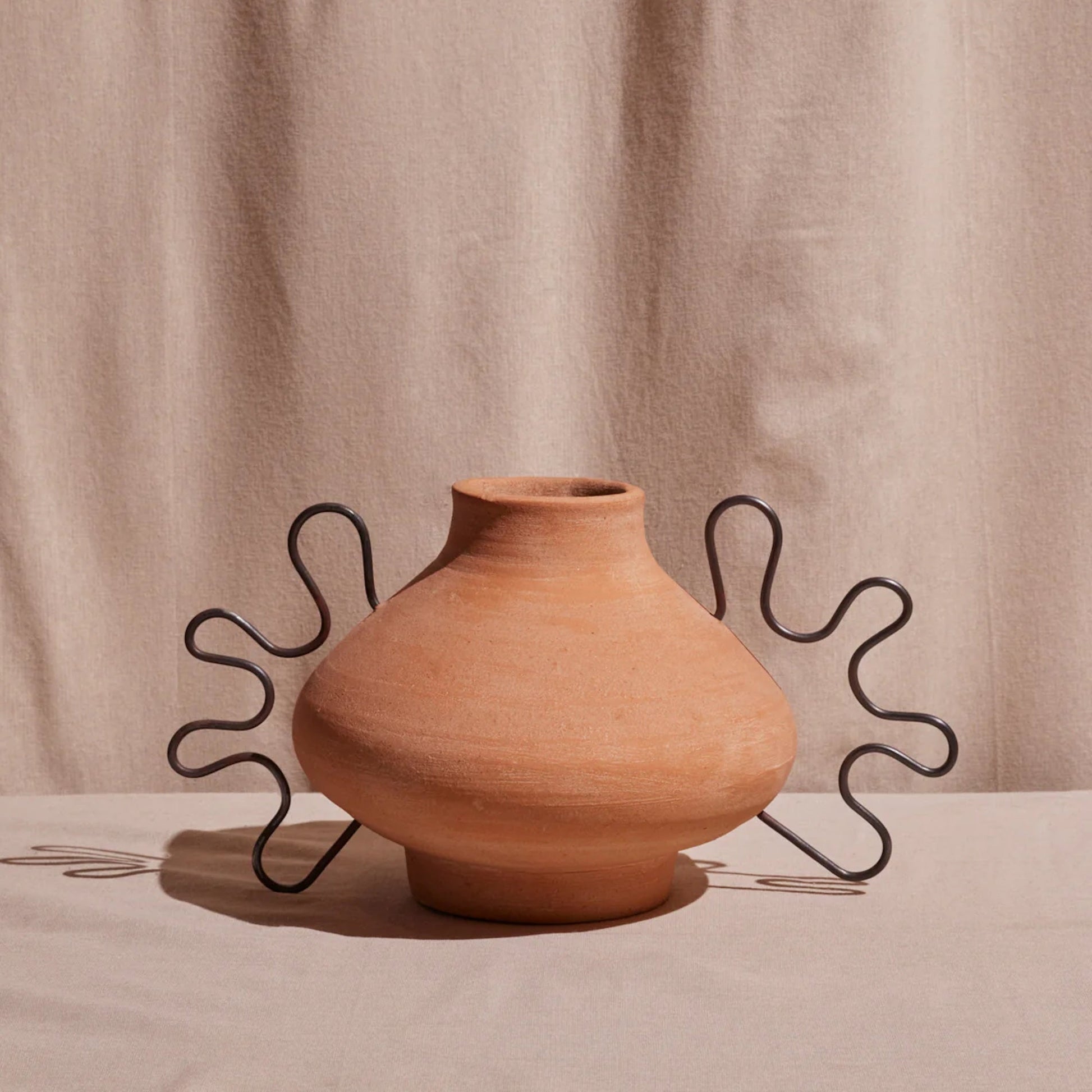 Terracotta vase with wavy metal stand on a beige background