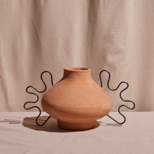 Terracotta vase with wavy metal stand on a beige background