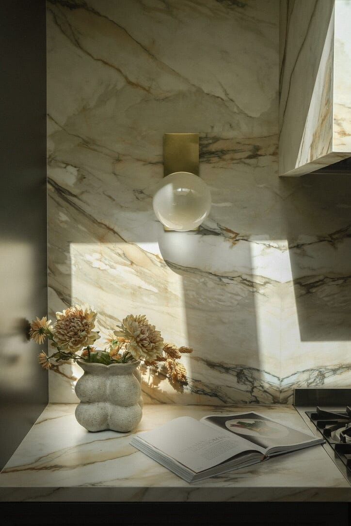 Decorative light fixture on a marble wall with a vase and book on a table below.