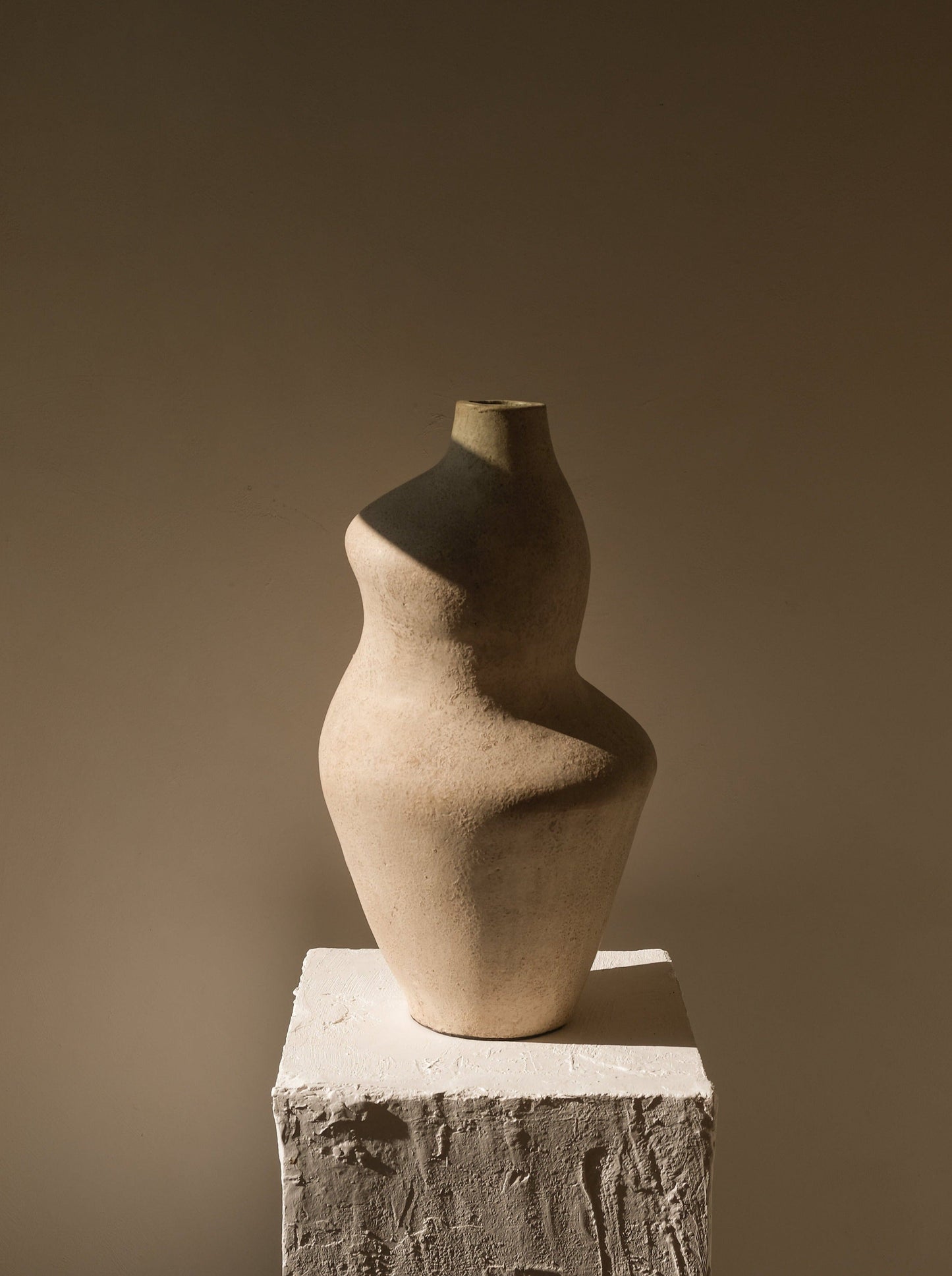 Ceramic vase on a textured pedestal against a brown background