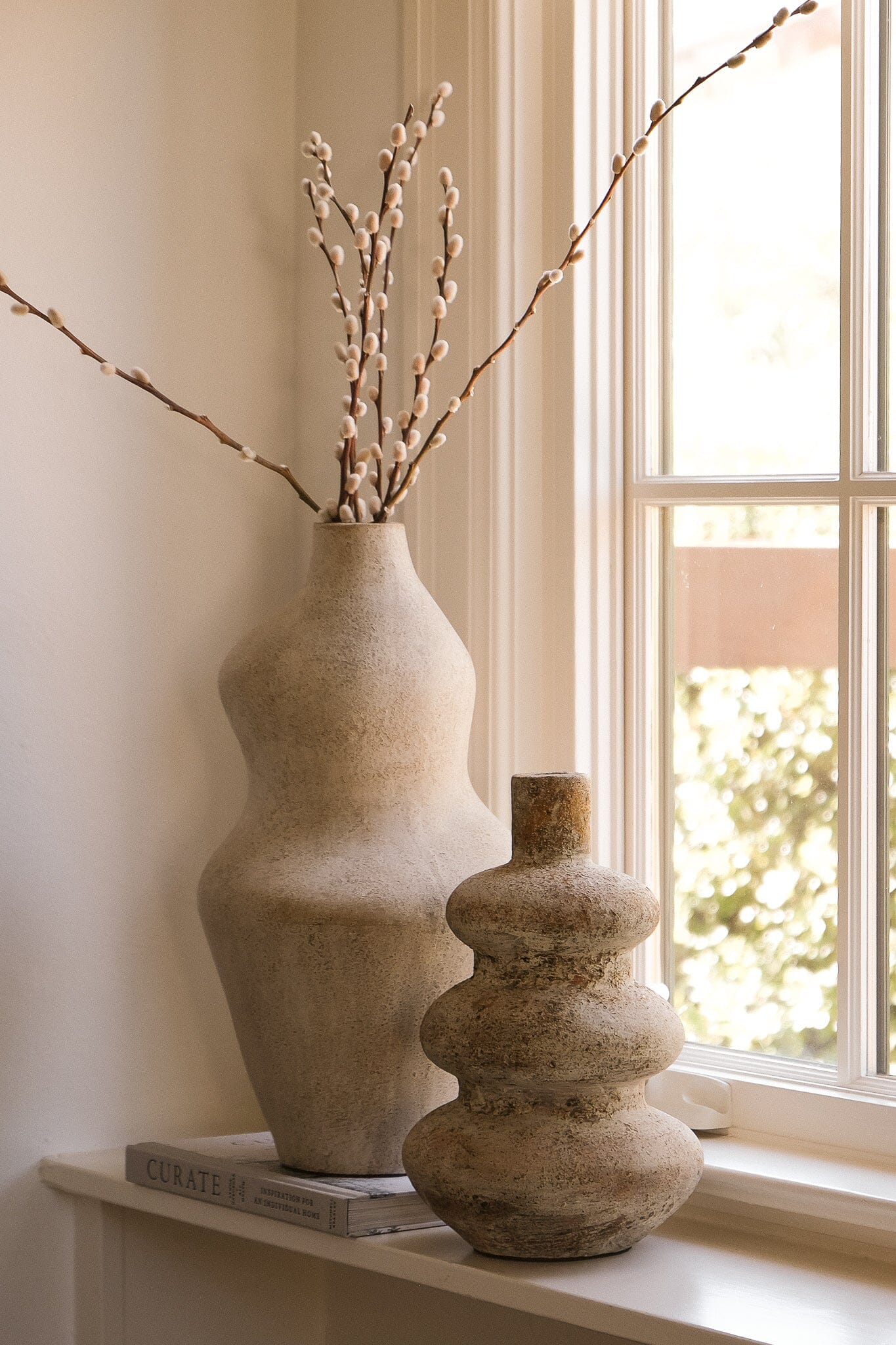 Two stone vases with branches on a windowsill