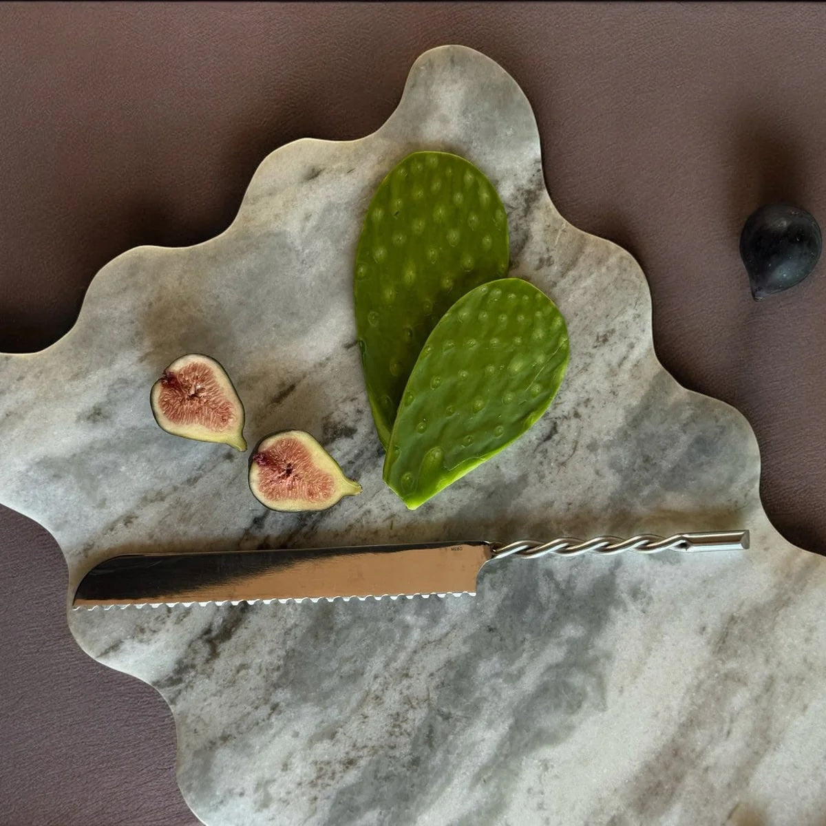 Marble cutting board with figs and a cactus leaf on a brown background