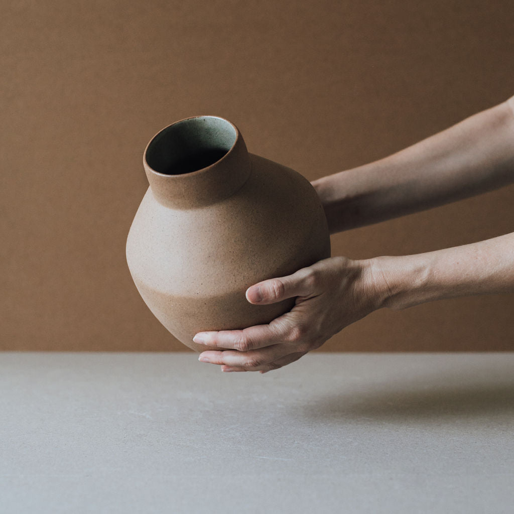 Person holding a brown ceramic vase against a neutral background