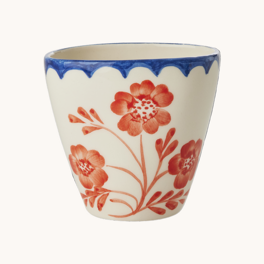 Ceramic cup with red floral design and blue rim on a white background