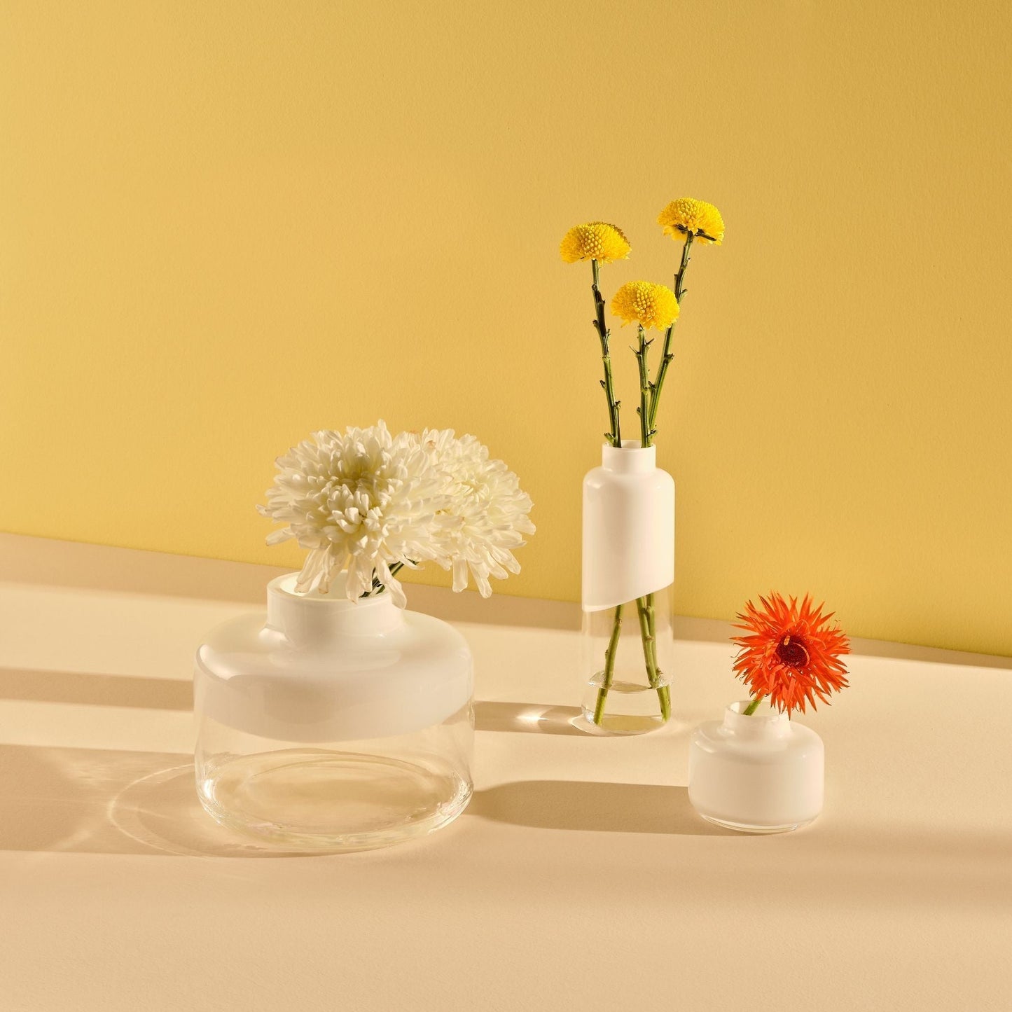 Three small white vases with flowers on a yellow and beige gradient background