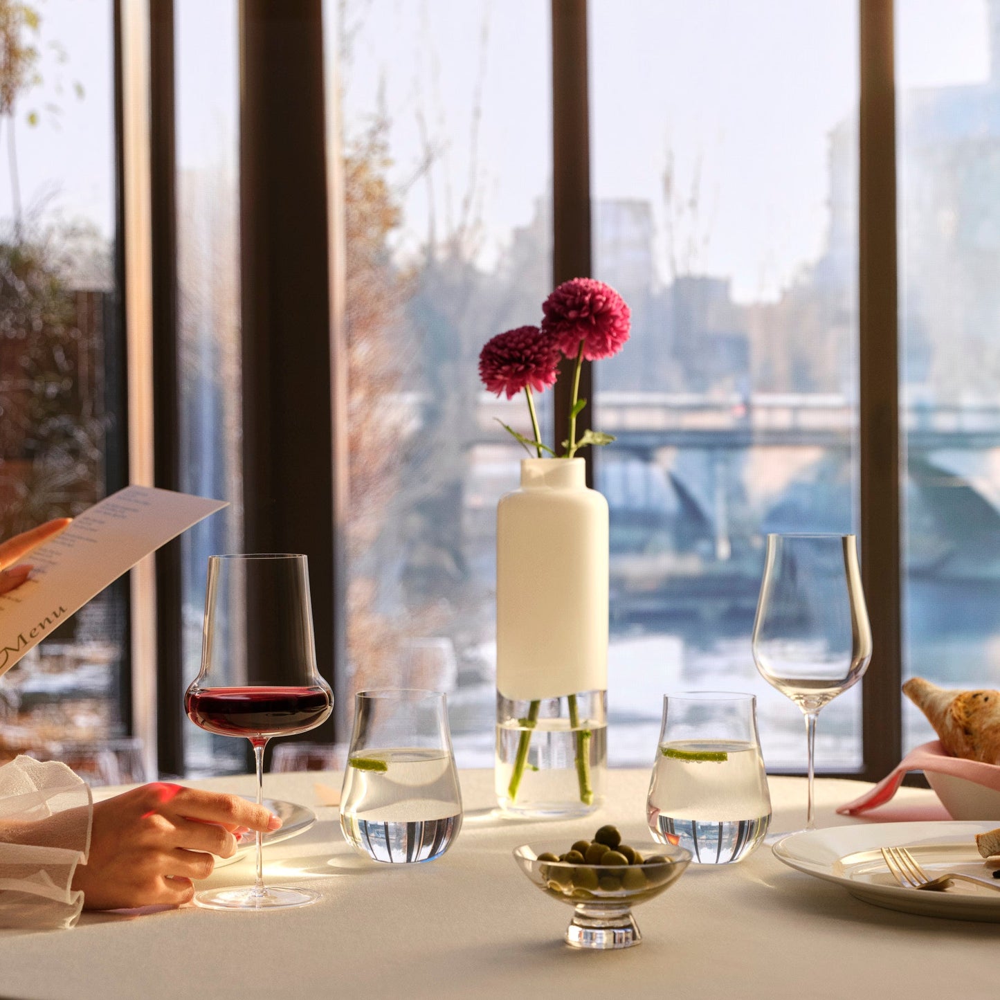 Dining table setup with wine glasses, a vase with flowers, and a menu in a restaurant setting.