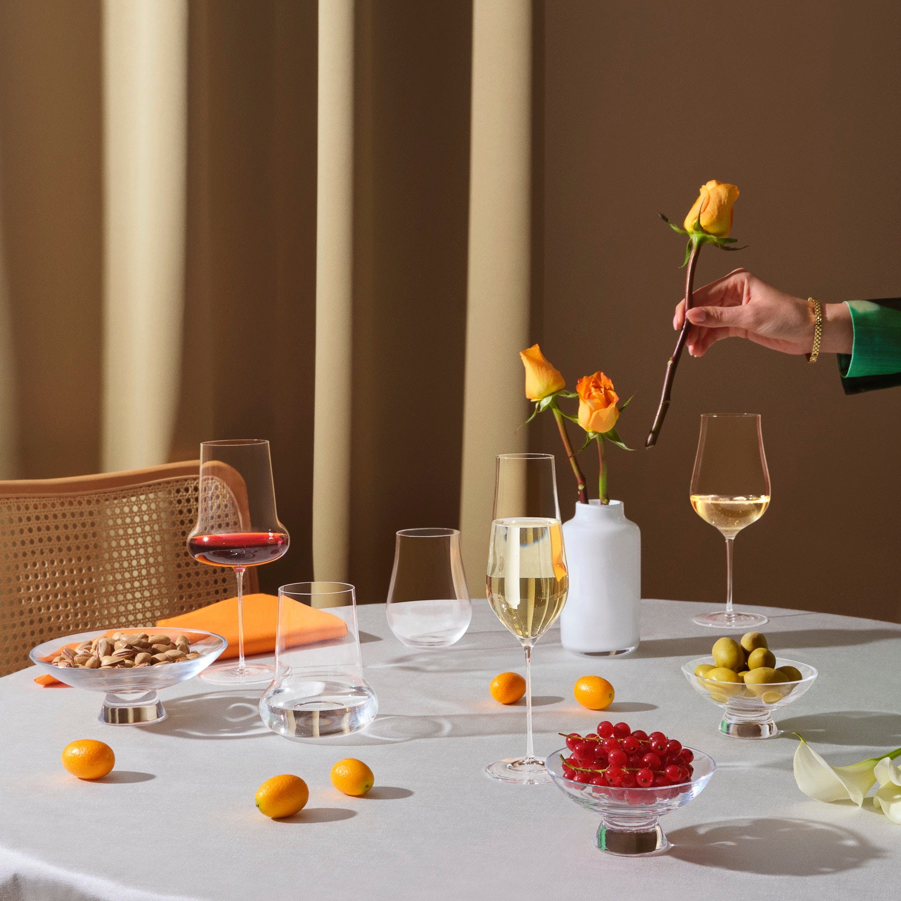Table setting with wine glasses, fruits, and a vase of flowers against a neutral background