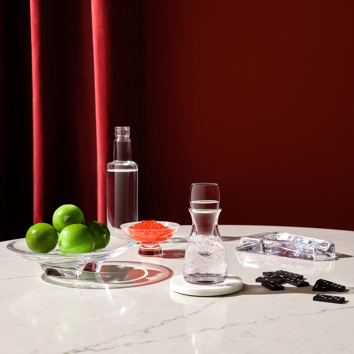 Clear glass carafe with water on a white surface with red curtain background
