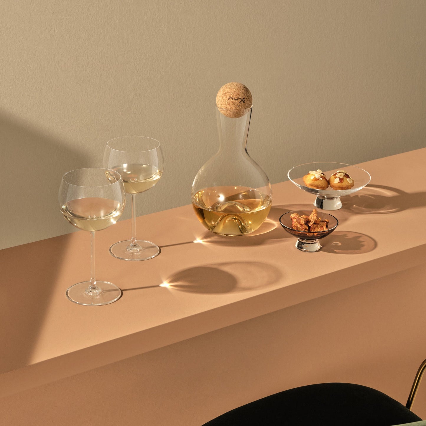 Wine glasses, decanter, and small plates with food on a beige surface