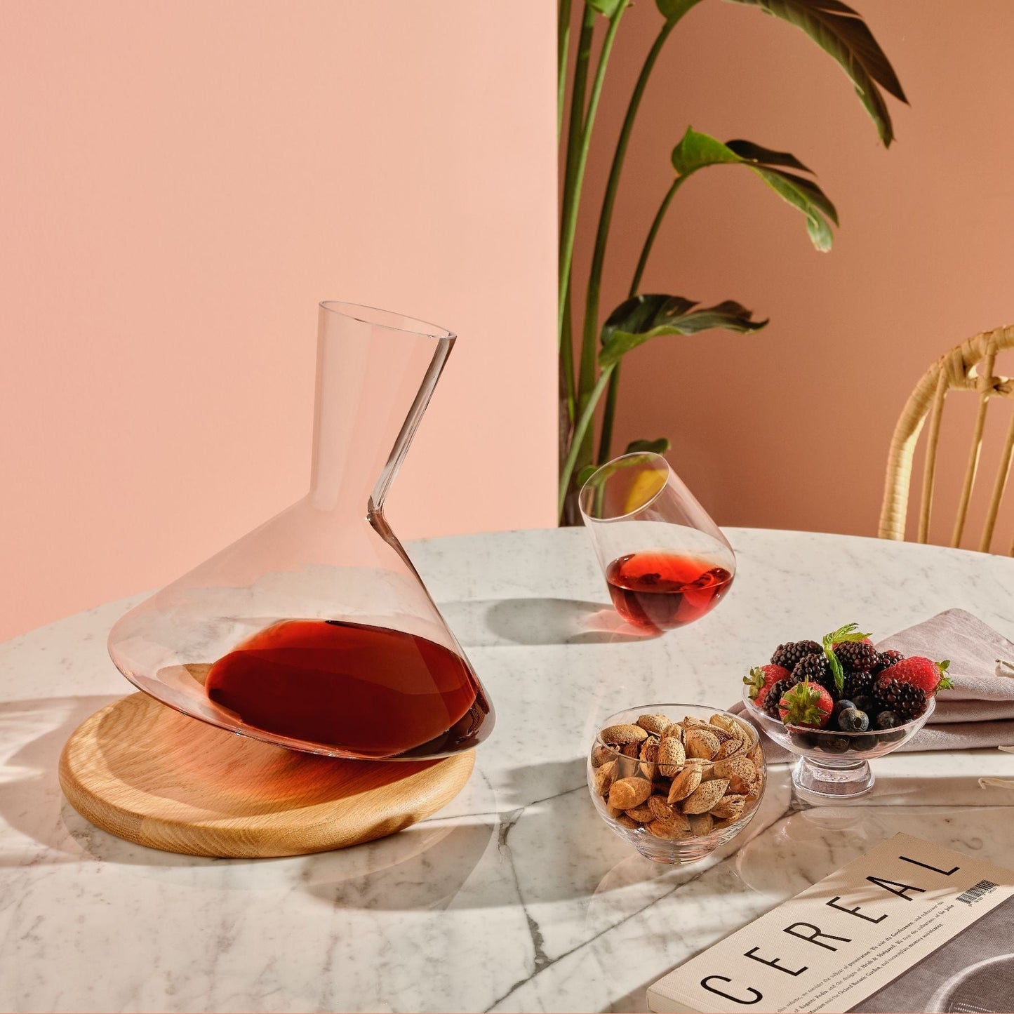 Glass decanter with red liquid on a marble table with a plant in the background
