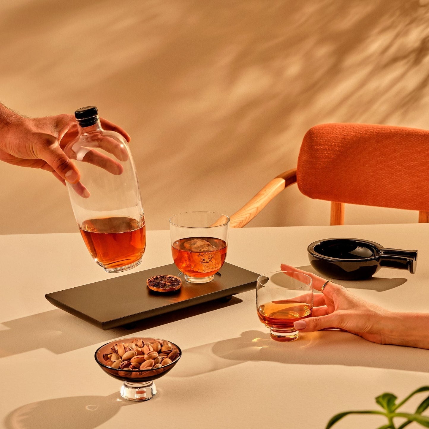 Two people sharing a bottle and glasses of amber liquid at a table with a warm, earthy background.