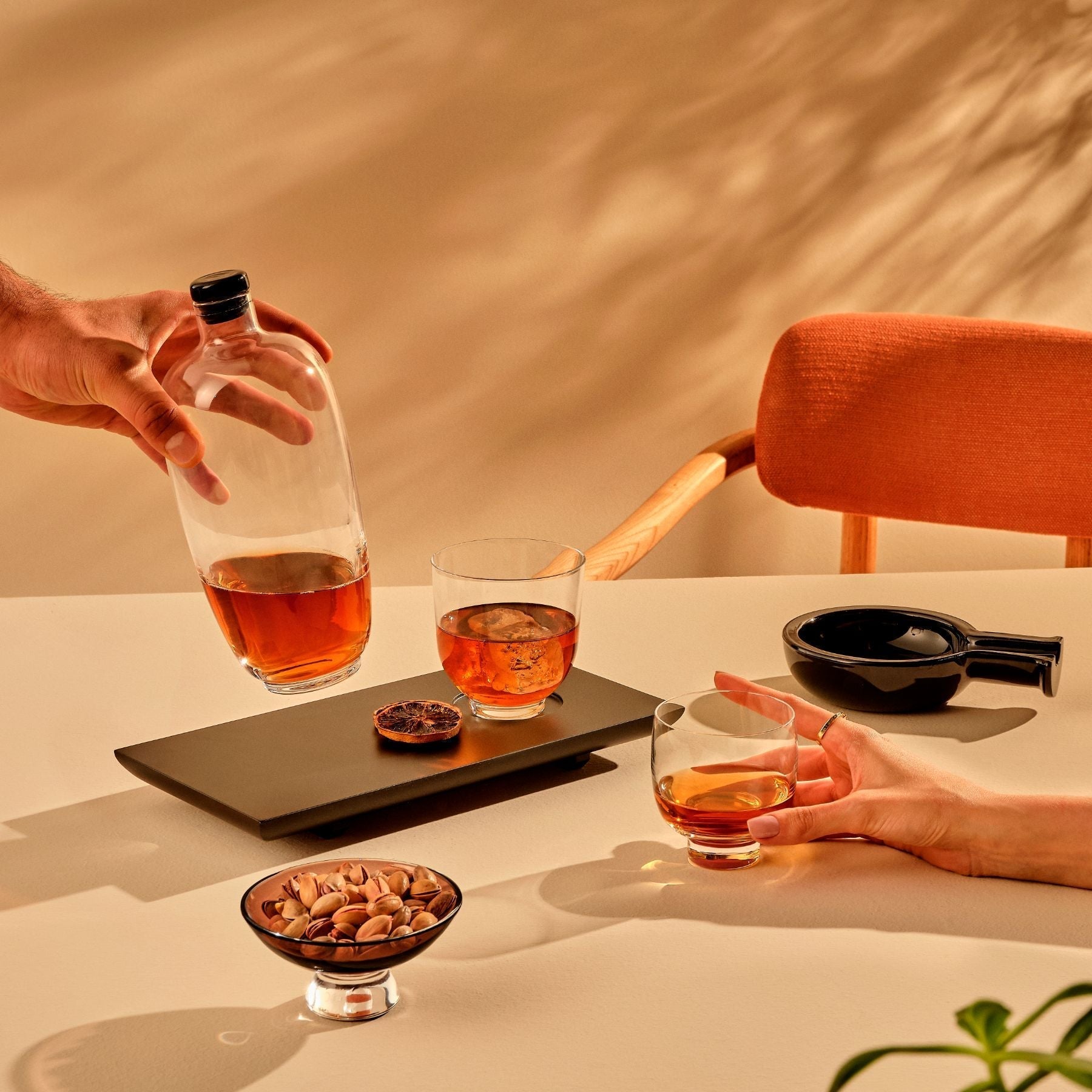 Two people sharing a bottle and glasses of amber liquid at a table with a warm, earthy background.