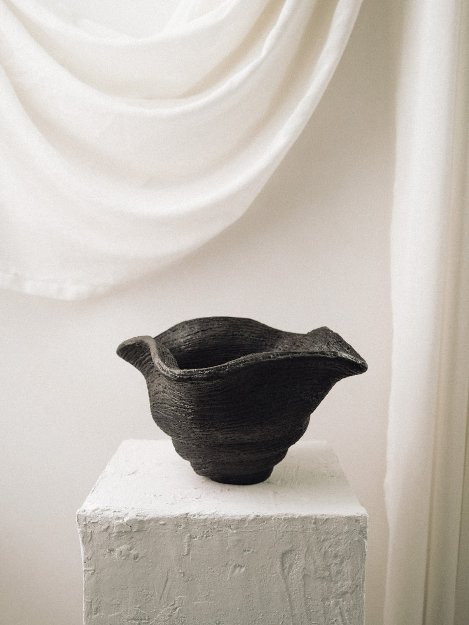 Black ceramic bowl on a white pedestal with a white curtain background
