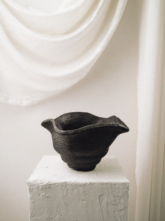 Black ceramic bowl on a white pedestal with a white curtain background