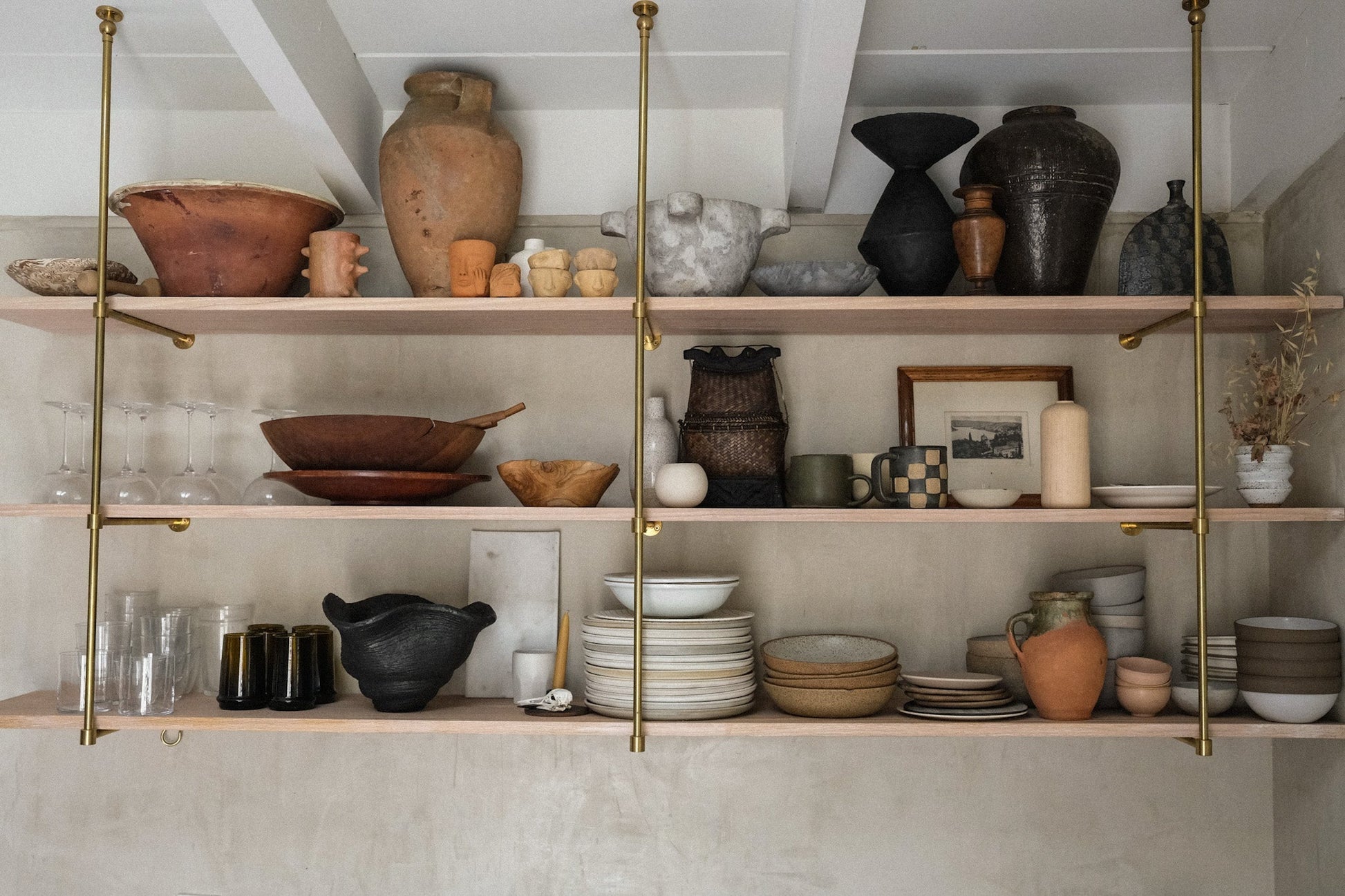 Shelves with various ceramic items in a room with white walls and wooden floor.